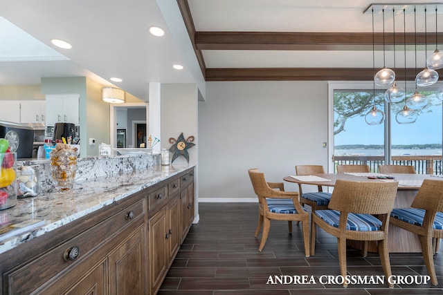 kitchen with white cabinetry, dark wood-type flooring, light stone counters, decorative light fixtures, and a water view