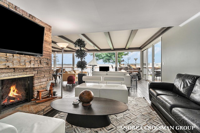 living room with beamed ceiling, light hardwood / wood-style floors, and a stone fireplace