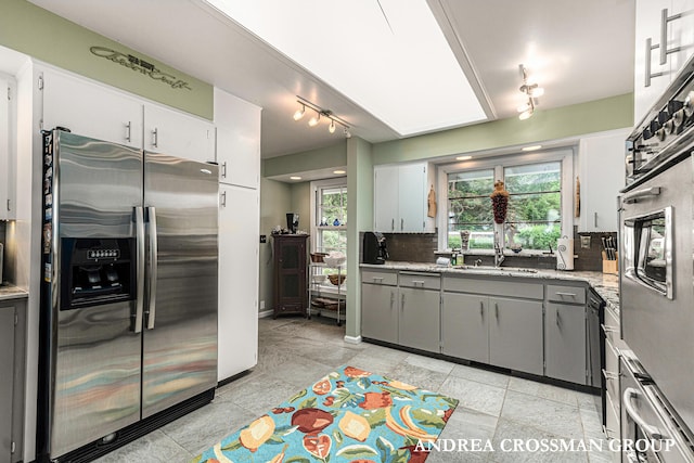 kitchen with gray cabinetry, decorative backsplash, sink, and stainless steel appliances