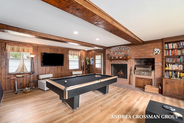 rec room with a brick fireplace, beamed ceiling, a healthy amount of sunlight, and light hardwood / wood-style floors