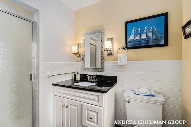 bathroom with vanity, toilet, a shower with shower door, and tile walls