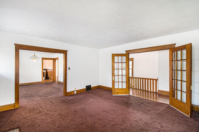 carpeted empty room with french doors, a textured ceiling, and a notable chandelier