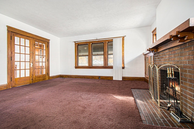 unfurnished living room featuring a textured ceiling, a fireplace, dark carpet, and french doors