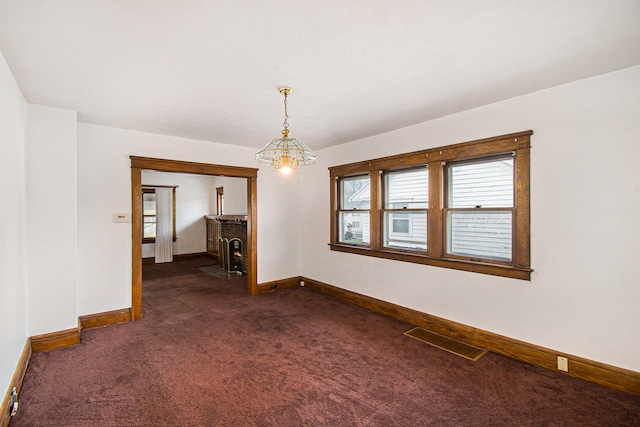 spare room featuring a notable chandelier and dark carpet