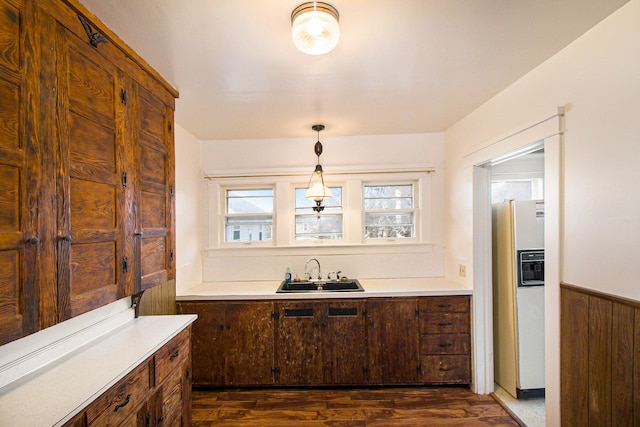 kitchen featuring sink, dark wood-type flooring, white refrigerator with ice dispenser, decorative light fixtures, and wooden walls