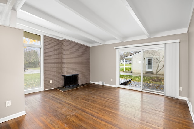 unfurnished living room with beam ceiling, plenty of natural light, dark hardwood / wood-style floors, and a brick fireplace