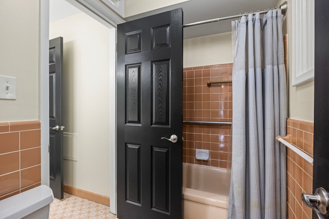 bathroom with tile patterned floors, shower / bathtub combination with curtain, toilet, and tile walls