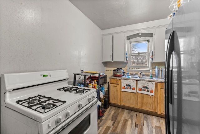 kitchen featuring white cabinets, sink, white gas range oven, stainless steel fridge, and wood-type flooring