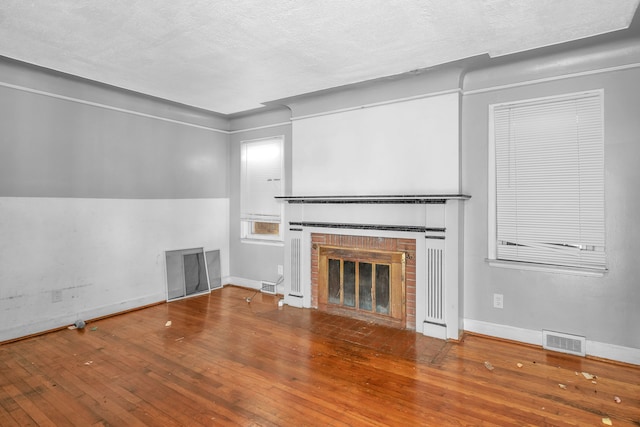 unfurnished living room with a brick fireplace, hardwood / wood-style floors, and a textured ceiling