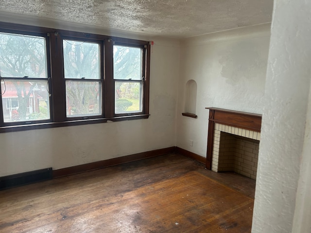 unfurnished living room featuring dark hardwood / wood-style floors, a textured ceiling, and a brick fireplace