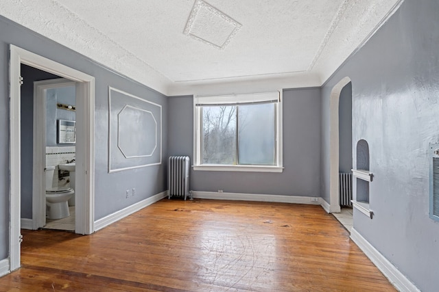 1055 Philip St, Detroit, MI 48215 - unfurnished bedroom featuring radiator heating unit, wood-type flooring, a textured ceiling, arched walkways, and ensuite bath