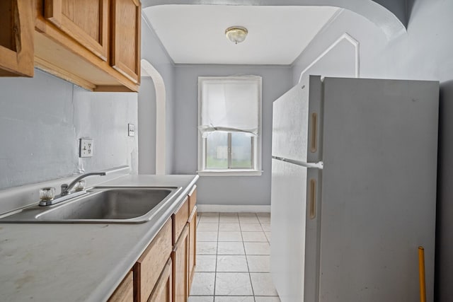 kitchen with light tile patterned floors, white fridge, and sink