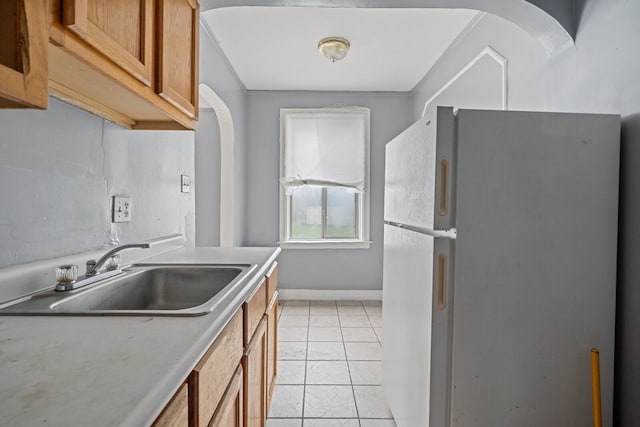1055 Philip St, Detroit, MI 48215 - kitchen featuring freestanding refrigerator, a sink, brown cabinetry, light tile patterned flooring, and arched walkways