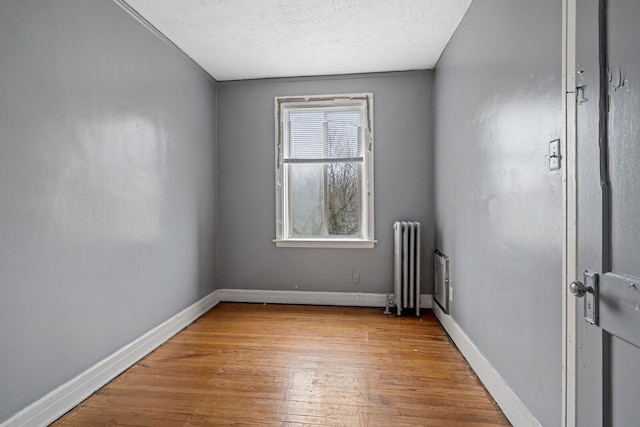 empty room featuring radiator, light hardwood / wood-style flooring, a textured ceiling, and ornamental molding