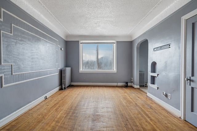 unfurnished room with light wood-type flooring, radiator heating unit, and a textured ceiling