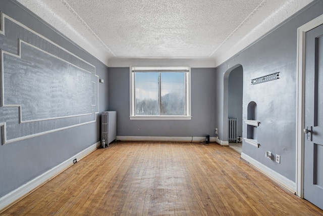 1055 Philip St, Detroit, MI 48215 - spare room with radiator heating unit, arched walkways, a textured ceiling, wood finished floors, and baseboards