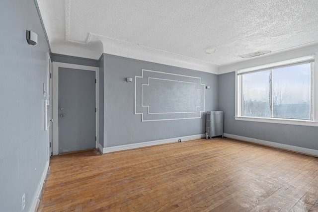 empty room with radiator heating unit, light wood-type flooring, and a textured ceiling