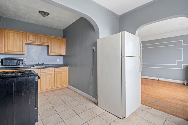 kitchen featuring white fridge, black stove, light hardwood / wood-style floors, and light brown cabinetry