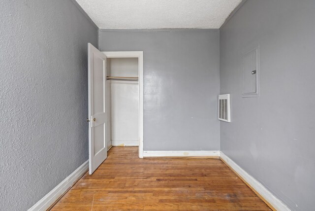 1055 Philip St, Detroit, MI 48215 - unfurnished bedroom featuring electric panel, wood finished floors, baseboards, a textured ceiling, and a textured wall
