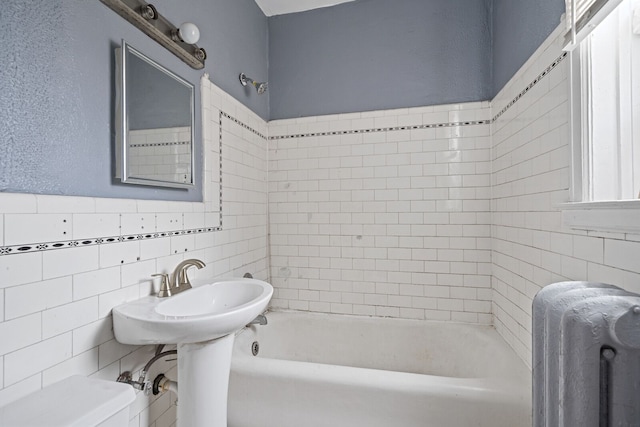 bathroom with radiator, tiled shower / bath combo, tile walls, and toilet