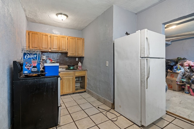 kitchen with white fridge, light tile patterned flooring, a textured ceiling, and tasteful backsplash