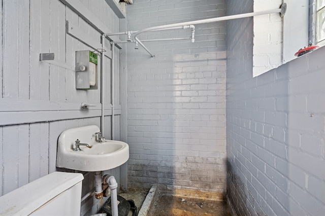 bathroom featuring toilet and brick wall