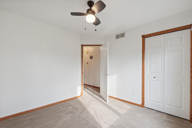 unfurnished bedroom with a closet, light colored carpet, and ceiling fan