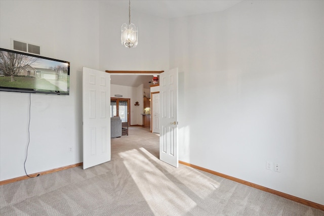 spare room featuring light carpet, a towering ceiling, and an inviting chandelier