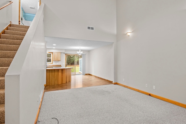 5279 Vinton Rd, Williamsburg, MI 49690 - unfurnished living room featuring light colored carpet, a chandelier, baseboards, stairs, and a high ceiling