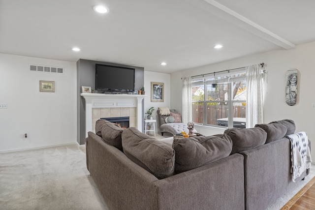 carpeted living room with a tile fireplace and beamed ceiling