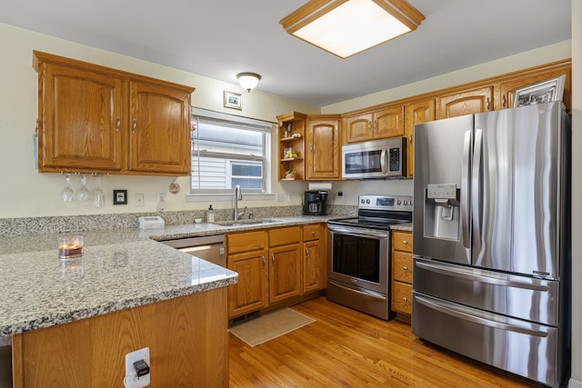 kitchen with sink, light stone counters, light hardwood / wood-style flooring, kitchen peninsula, and appliances with stainless steel finishes