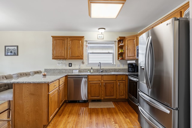 kitchen with kitchen peninsula, light stone counters, stainless steel appliances, light hardwood / wood-style floors, and a breakfast bar area