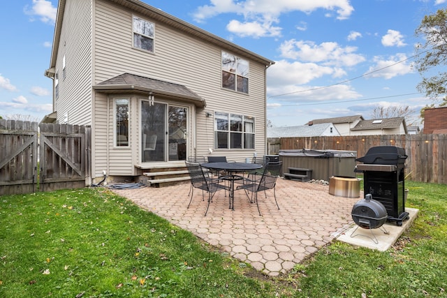 back of house featuring a hot tub, a patio area, and a lawn