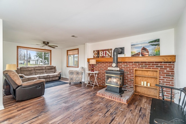 living room with hardwood / wood-style floors, a wood stove, and ceiling fan