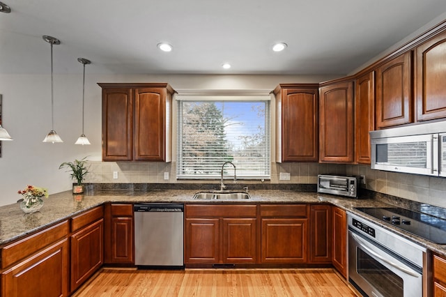 kitchen with backsplash, sink, hanging light fixtures, light wood-type flooring, and stainless steel appliances