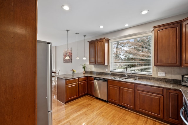 kitchen featuring kitchen peninsula, stainless steel appliances, sink, decorative light fixtures, and light hardwood / wood-style flooring