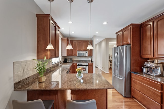 kitchen featuring kitchen peninsula, light wood-type flooring, stainless steel appliances, dark stone countertops, and hanging light fixtures