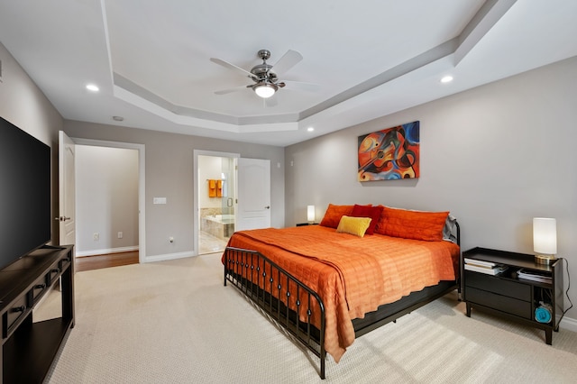 carpeted bedroom featuring connected bathroom, a tray ceiling, and ceiling fan