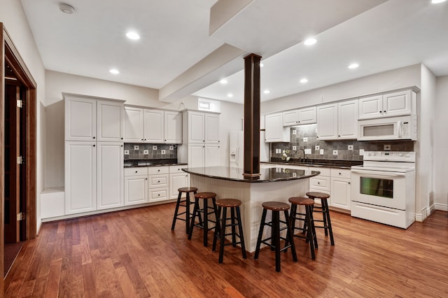 kitchen with white appliances, hardwood / wood-style flooring, tasteful backsplash, white cabinetry, and a breakfast bar area