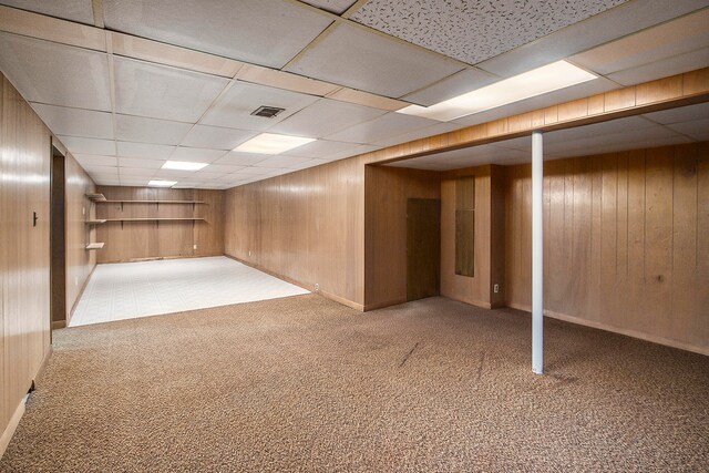 basement with a paneled ceiling, wooden walls, and carpet