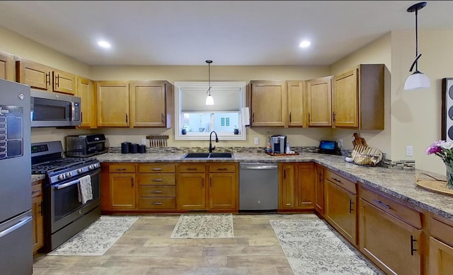 kitchen featuring stone countertops, a sink, hanging light fixtures, stainless steel appliances, and light wood finished floors