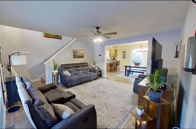 living area featuring ceiling fan with notable chandelier, light wood-style flooring, baseboards, and stairs