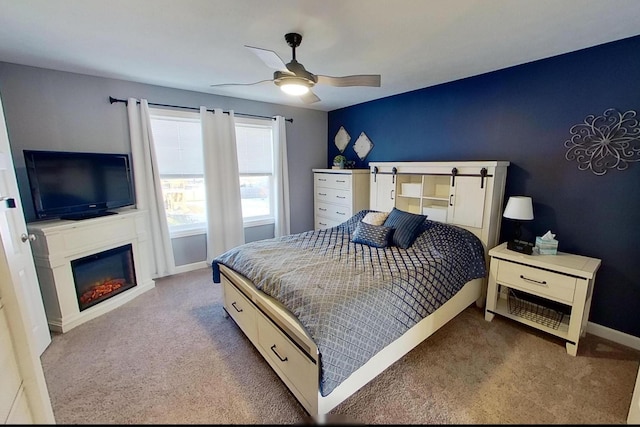 bedroom with ceiling fan, baseboards, a glass covered fireplace, and carpet floors