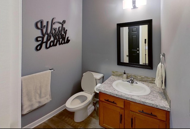 half bathroom with vanity, baseboards, toilet, and wood finished floors