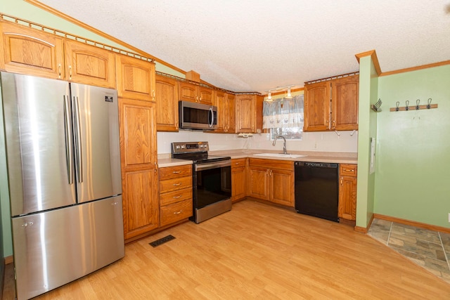 kitchen with a textured ceiling, light wood-type flooring, sink, and appliances with stainless steel finishes