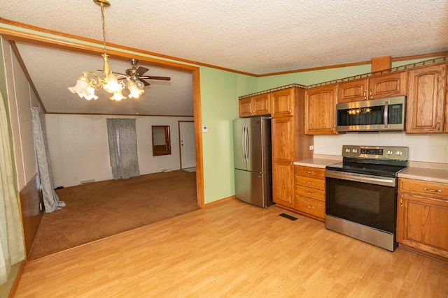 kitchen with appliances with stainless steel finishes, light wood-type flooring, a textured ceiling, vaulted ceiling, and hanging light fixtures