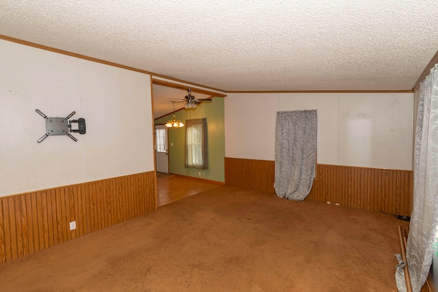 empty room featuring carpet flooring, a textured ceiling, wooden walls, and ornamental molding