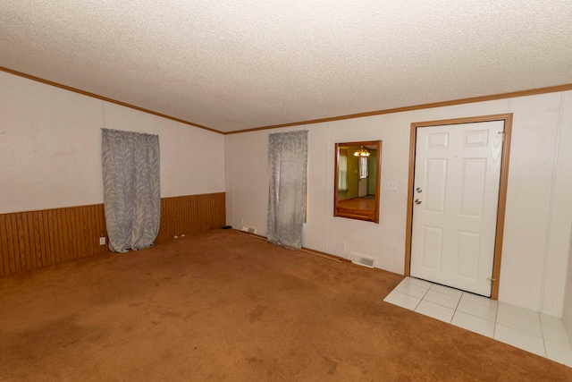 foyer featuring light carpet, crown molding, a textured ceiling, and wooden walls