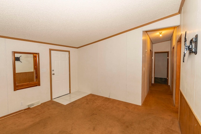 empty room with a textured ceiling, light colored carpet, vaulted ceiling, and ornamental molding