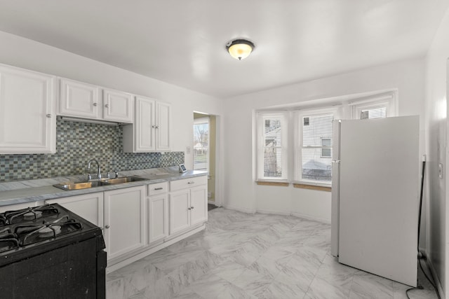 kitchen featuring backsplash, black range oven, sink, white fridge, and white cabinetry